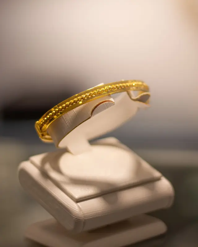 Textured gold bangle on a cream display stand