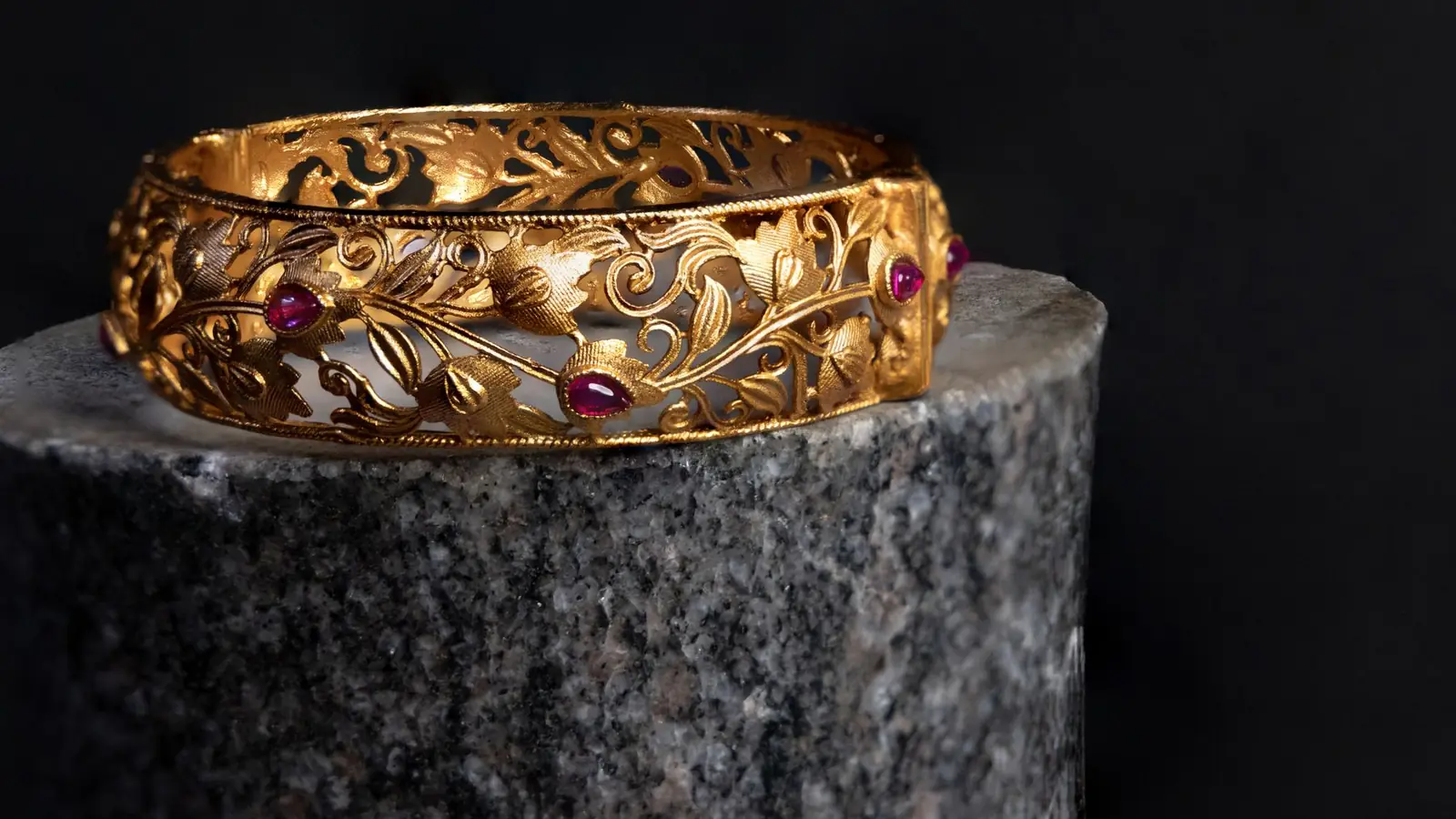 Gold filigree cuff with garnet stones resting on dark granite