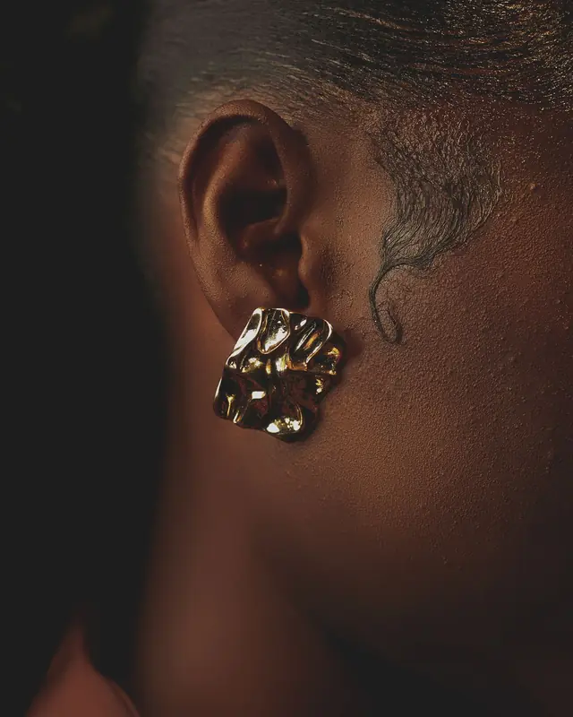 Sculptural gold earring against a dark background